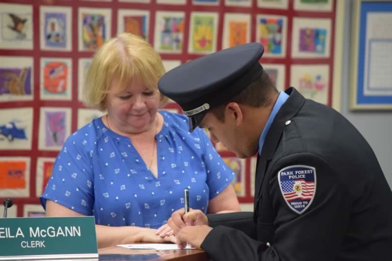 Newly sworn-in Officer Luis Ibarra signs his oath before Village Clerk Sheila McGann