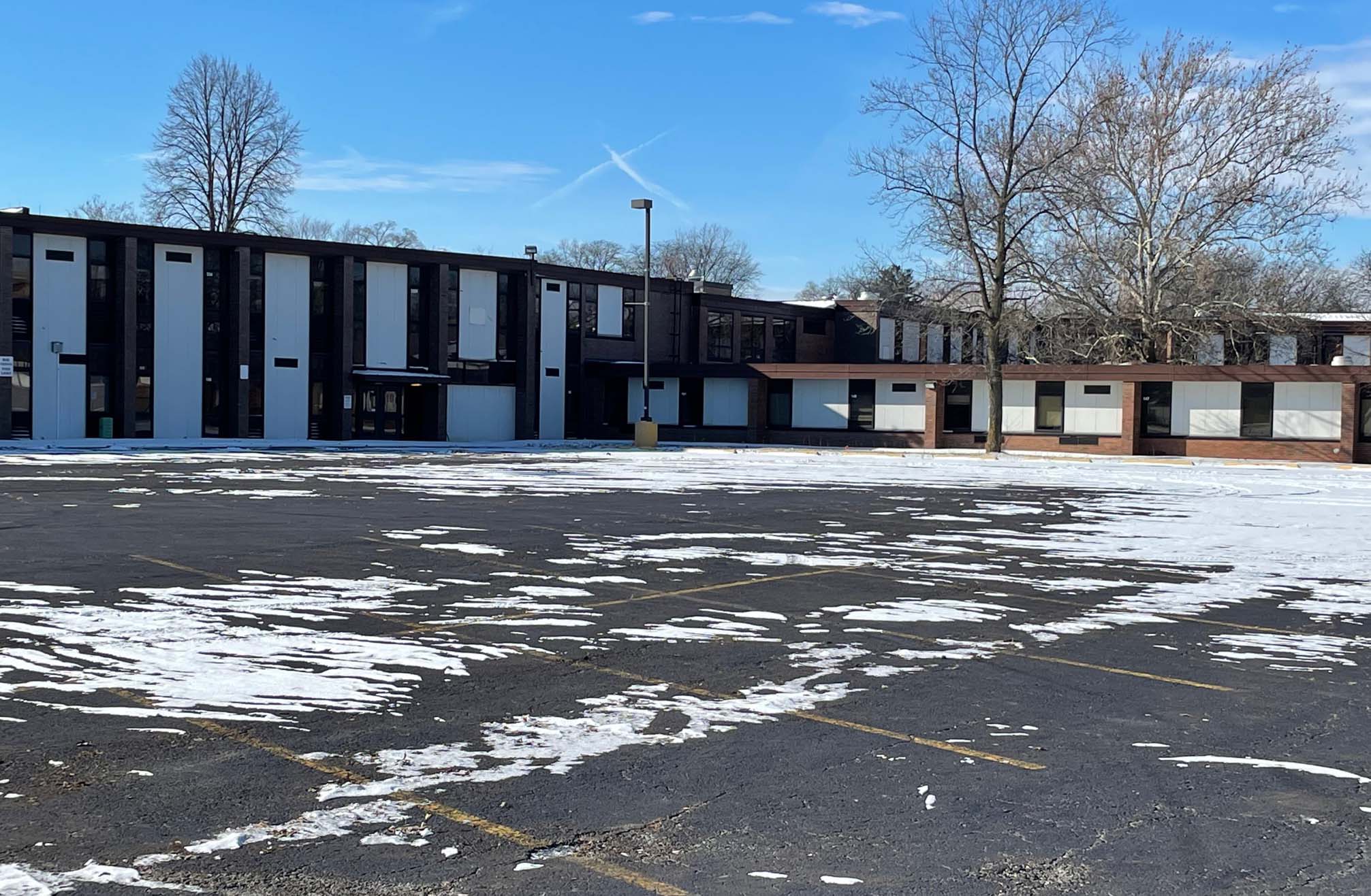 parking lot partially covered in snow with school building in the background