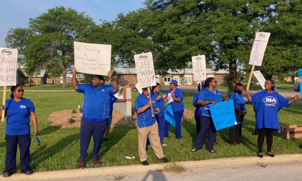 people wearing blue shirts hold picket signs along the street