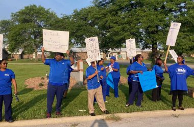 people wearing blue shirts hold picket signs along the street