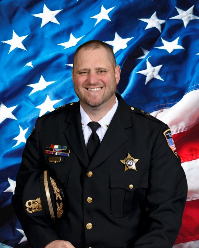 police officer with hat under his arm standing in front of American flag