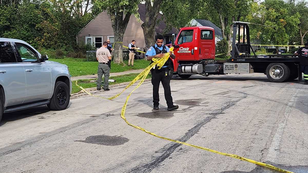 A Park Forest officer gathers crime tape while other local and State Police discuss the incident. (Gary Kopycinski)