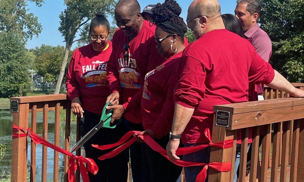 group of people standing on a bridge with a man cutting a ribbon