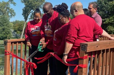 group of people standing on a bridge with a man cutting a ribbon